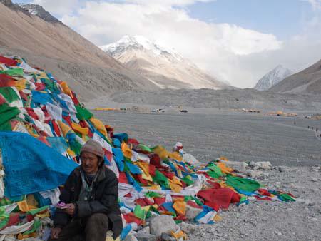 Tibetan next to some prayer flags with a cloud covered Everest in the background